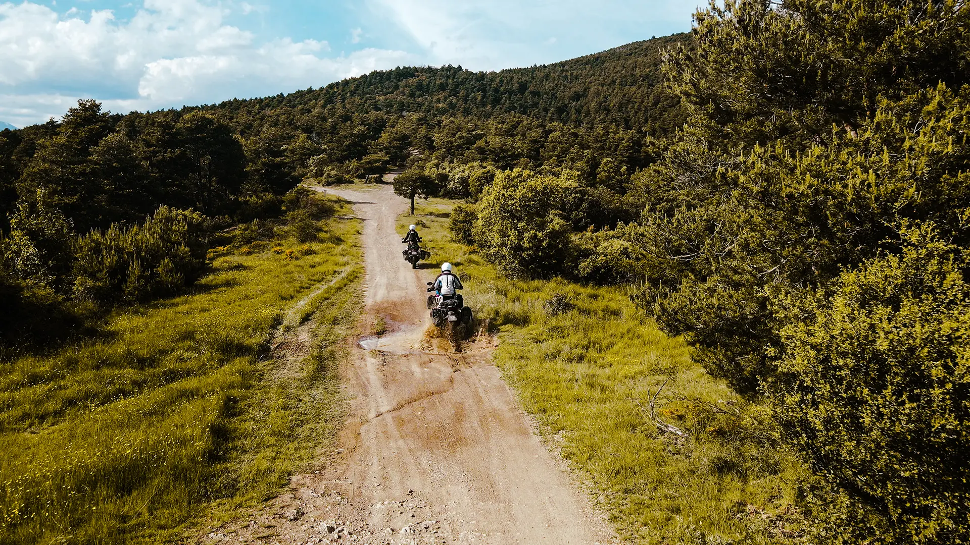 Moto Honda Africa Twin franchissant une large flaque d'eau sur une piste forestière des Pyrénées.