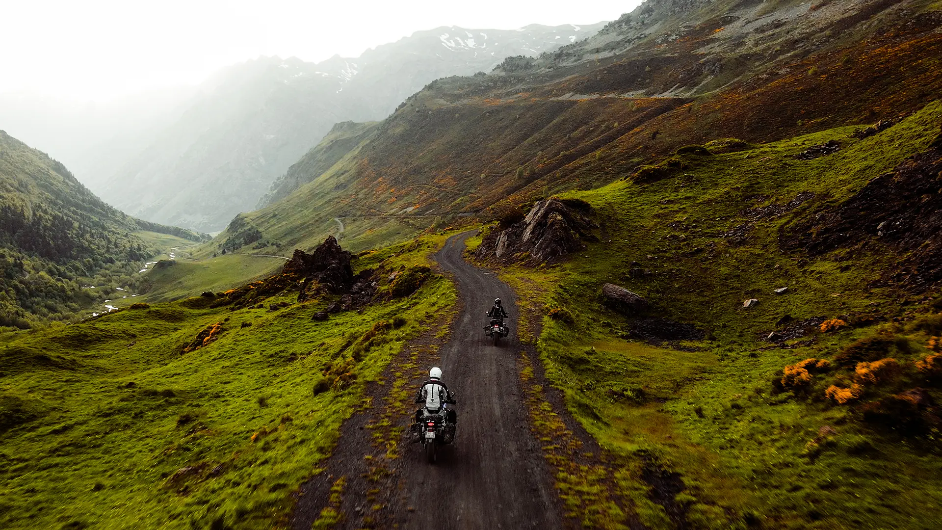 Deux motards en randonnée trail sur une piste sinueuse au cœur d'une vallée sauvage des Pyrénées.