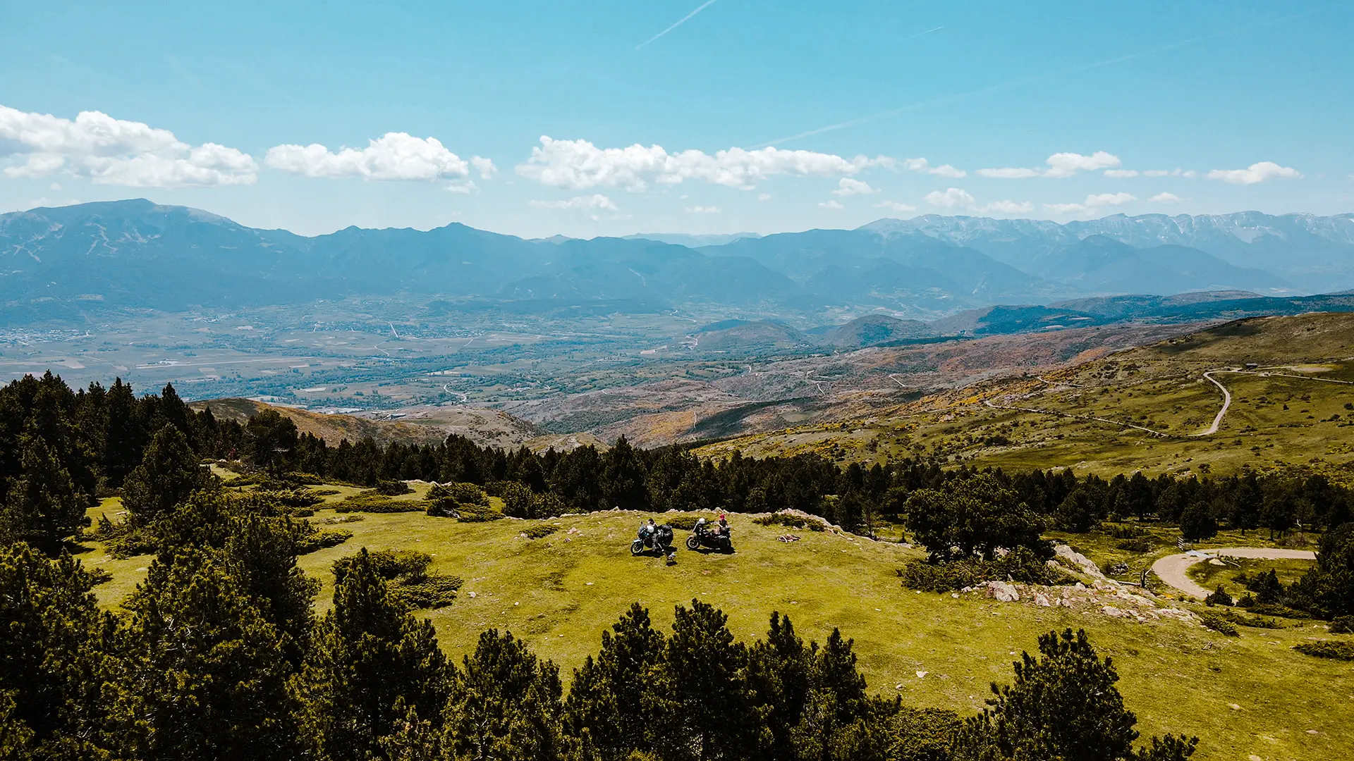 Deux motos trail garées sur un promontoire herbeux face au panorama des montagnes pyrénéennes.