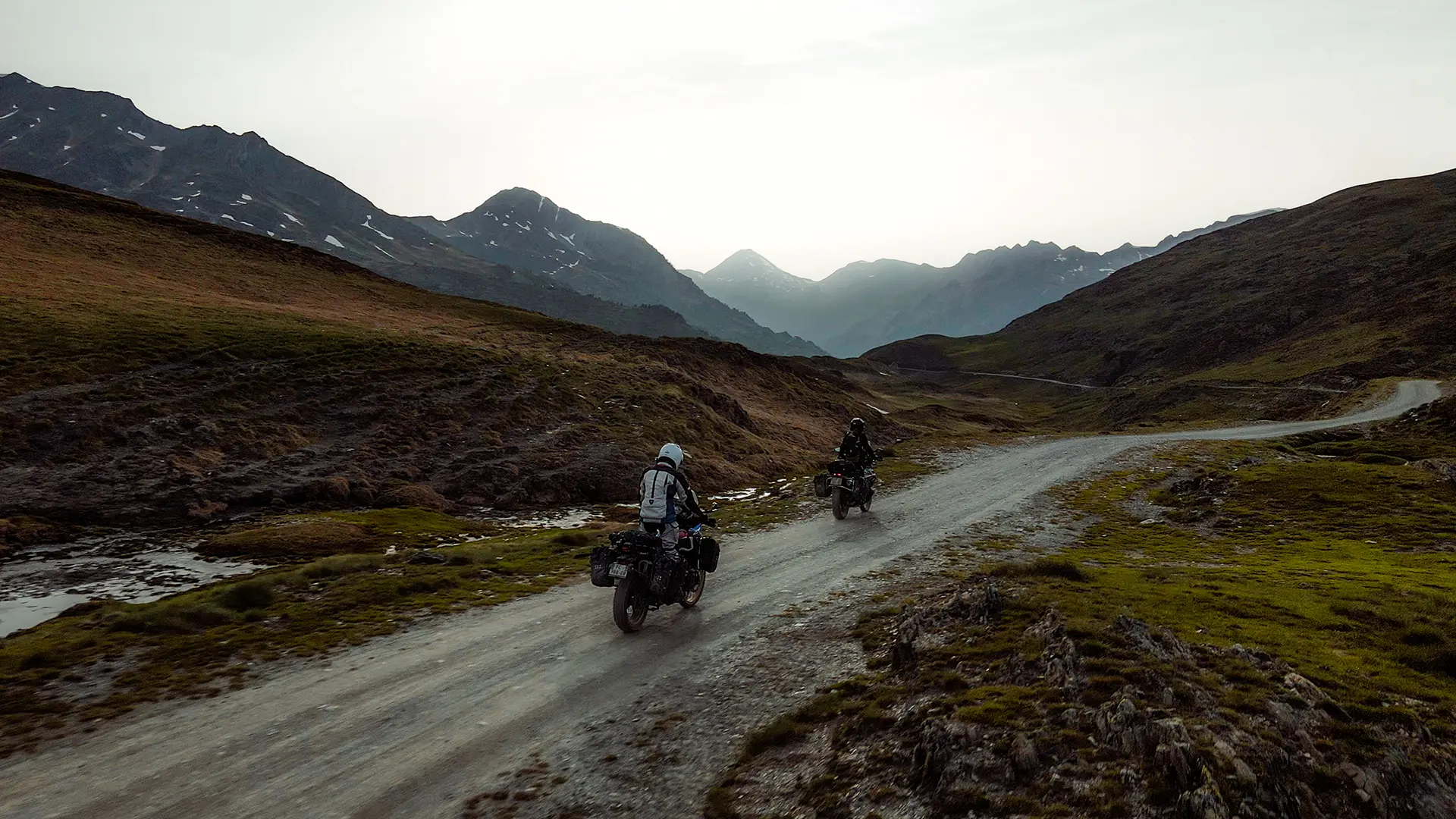 Deux motards roulant sur une piste de haute altitude dans un paysage de montagne rocailleux.